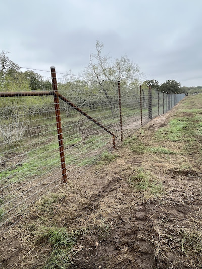 A long wire fence with metal posts, installed by the top-rated fencing company, runs across grassy terrain, with trees and a cloudy sky in the background.