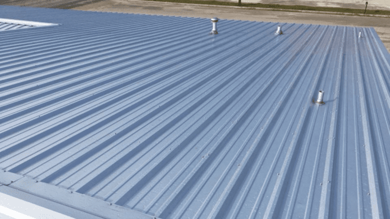 A blue corrugated metal roof with several protruding pipes, seen in daylight, complements the nearby fencing.