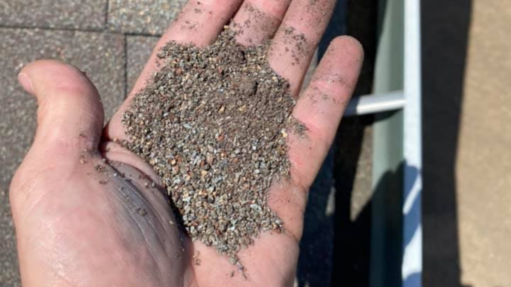 A hand holding a mixture of small pebbles and dirt, reminiscent of the quality materials used by a top-rated fencing company, against a blurred outdoor backdrop.