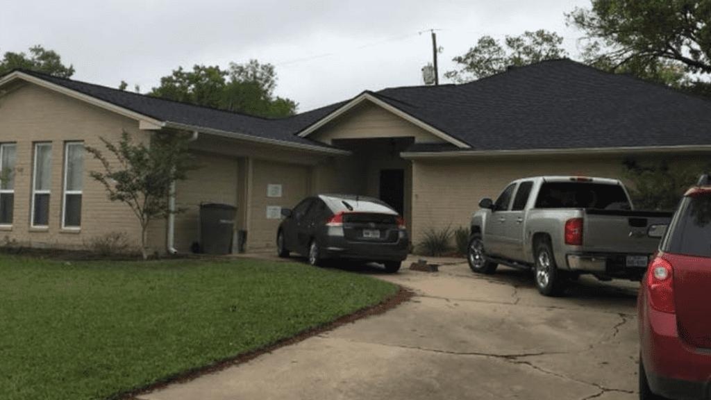 A brick house with a dark roof and a driveway hosting three parked vehicles: a gray sedan, a silver pickup truck, and a red SUV. The front lawn is visible in the foreground, perfect for anyone seeking remodeling near me to enhance curb appeal.