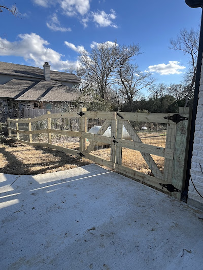 A beautifully crafted wooden fence, complete with a gate, surrounds the yard of a charming white brick house. As trees sway under a cloudy sky, consider how professional remodeling near you could enhance such classic appeal.