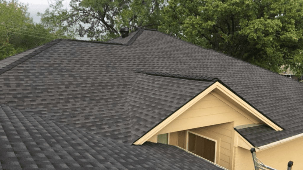 A house roof with dark gray shingles, expertly crafted by a top rated roofing company, nestled among lush green leafy trees.
