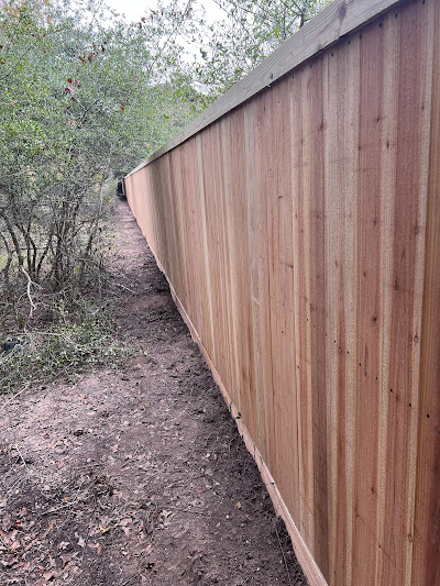 A tall wooden fence, expertly crafted by a top-rated fencing company, is lined with trees on one side and extends into the distance.