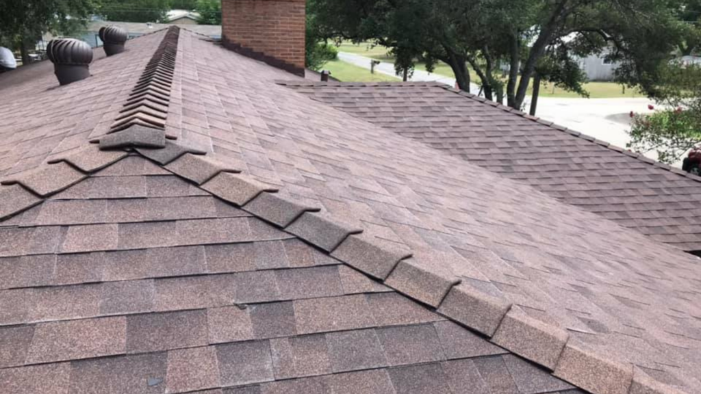 A sloped, shingled roof, crafted by a top-rated roofing company, boasts a brick chimney and multiple vents. Tree branches frame the scene in the background.