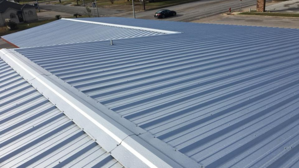 Elevated close-up of a metal roof with ridged panels, expertly installed by a top-rated roofing company. Streets and a car weave into the background.