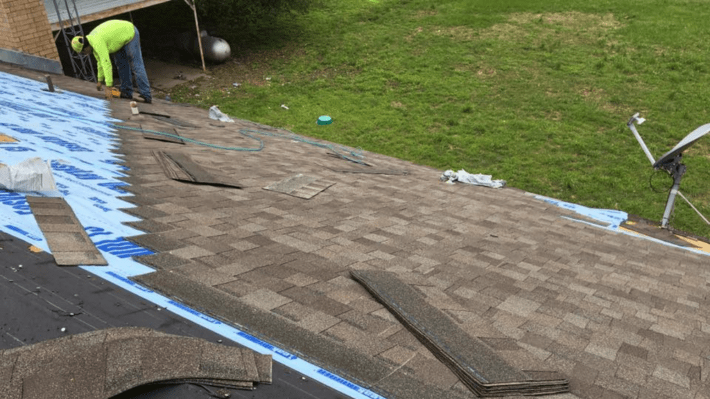 A worker in a neon green shirt, representing a top rated roofing company, installs shingles on a partially completed roof. Tools and materials are scattered around, while a grassy area is visible in the background.